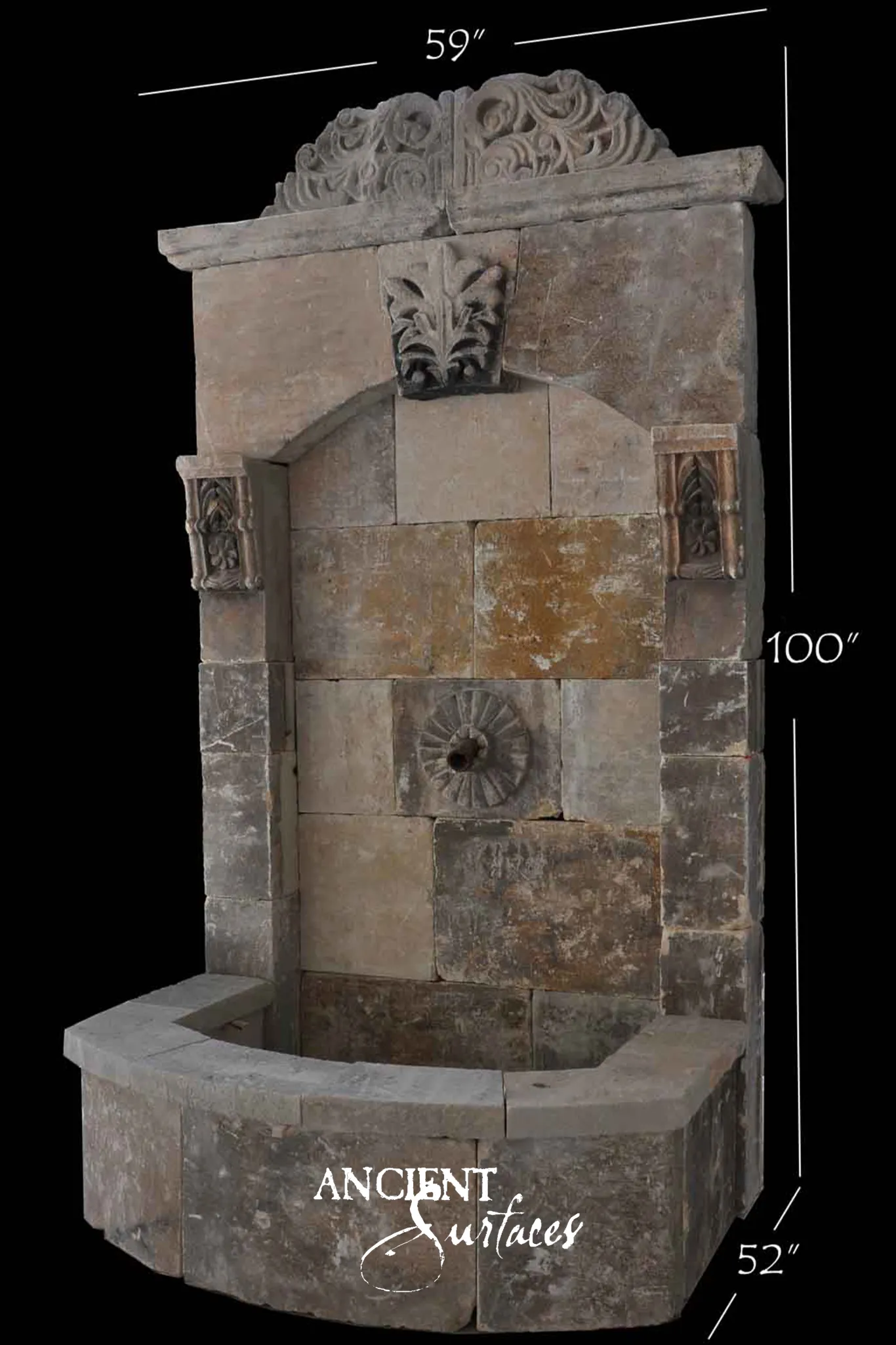 Reclaimed antique limestone wall fountain from Ancient Surfaces with a carved open scrollwork crest, an acanthus keystone over an arched niche, two carved bracket corbels, a rosette boss with a bronze spout and a canted apron basin