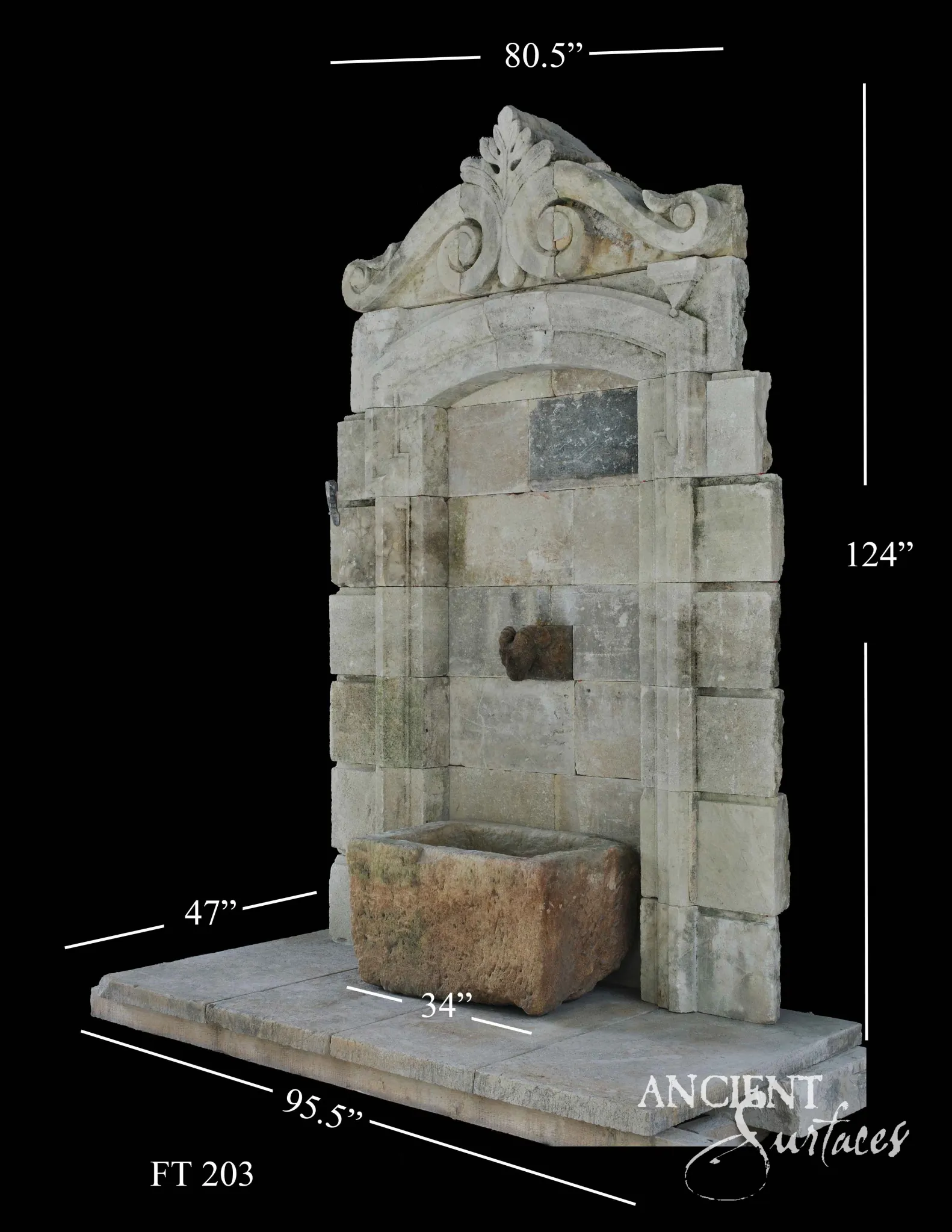 Monumental reclaimed antique limestone wall fountain from Ancient Surfaces standing over ten feet high, with a carved volute and acanthus crest above an arched ashlar niche, rusticated side piers and a small trough on a paved stone plinth