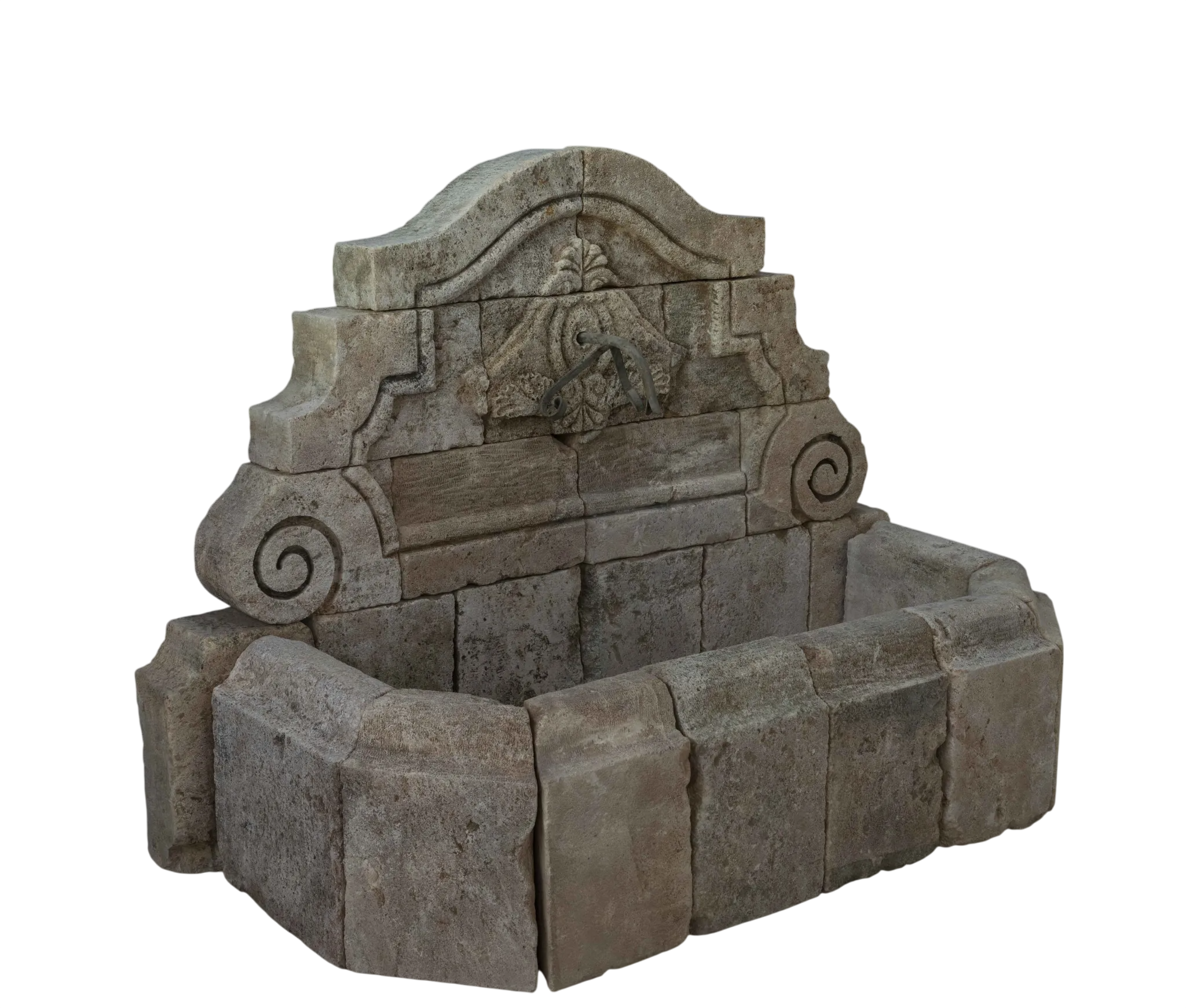Low broad reclaimed antique limestone wall fountain from Ancient Surfaces in warm pink buff stone, a carved shell and foliate cartouche in the arched crest between scrolled wings and large spiral volutes above a wide canted apron basin