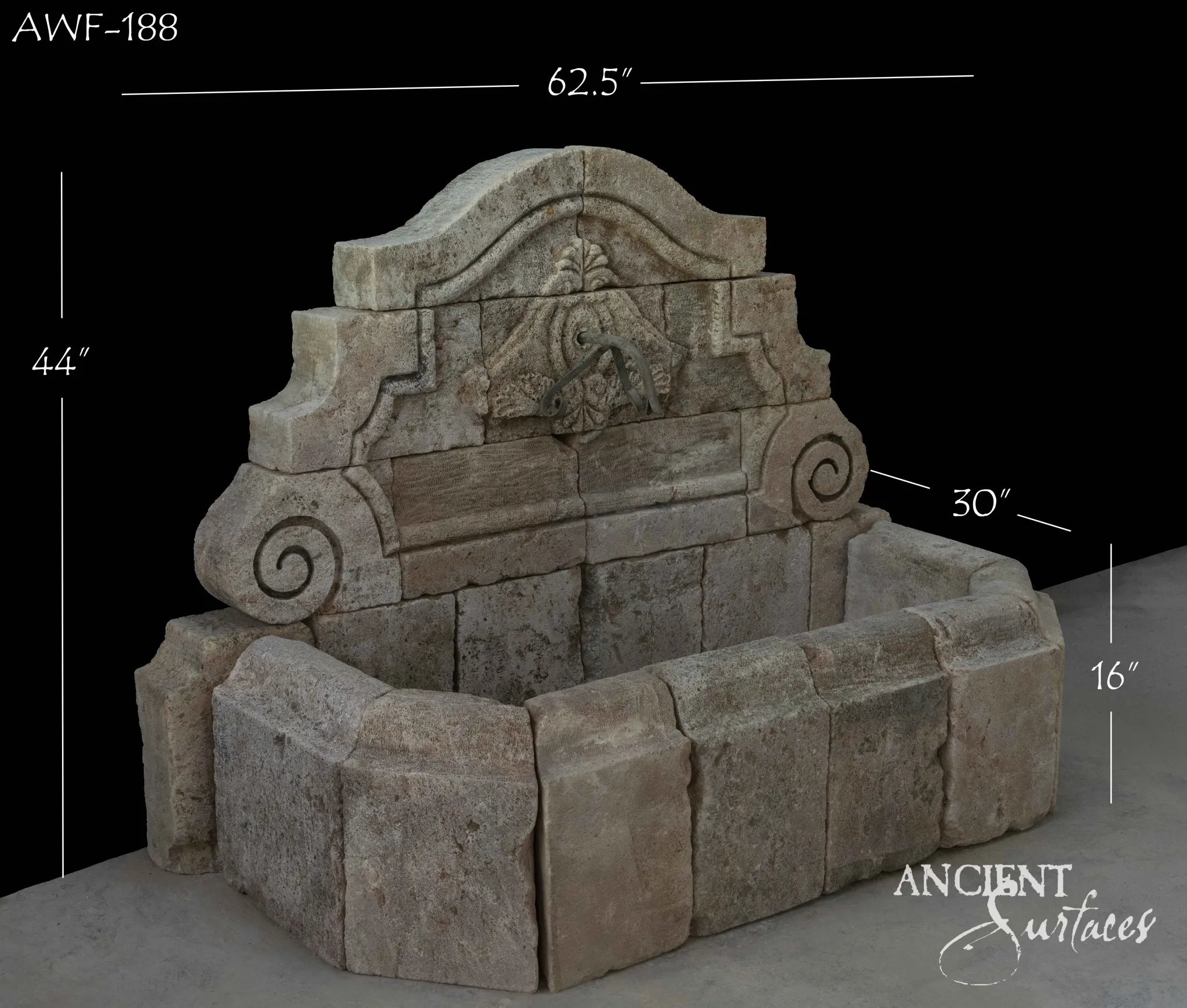 Low broad reclaimed antique limestone wall fountain from Ancient Surfaces in warm pink buff stone, a shell and foliate cartouche in the arched crest between scrolled wings and large spiral volutes, over a wide canted apron basin