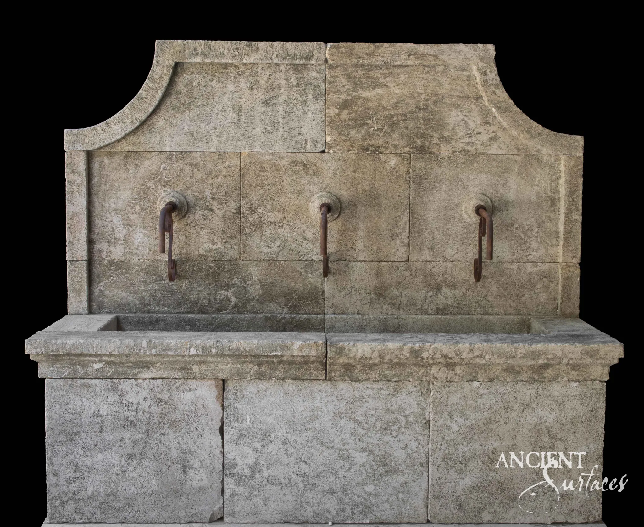 Wide reclaimed antique limestone wall fountain from Ancient Surfaces with three carved circular bosses each carrying a heavy iron hook spout, an ogee profiled top edge and a long flat coped stone trough